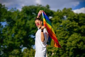 junge frau, die lgbt-stolzfahne im park schwenkt. foto