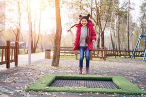 glückliches Schulmädchen, das auf einem kleinen Trampolin im Park springt foto