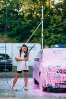 frau mit hochdruckschlauch steht mit rosa schaumstoff bedecktem auto foto