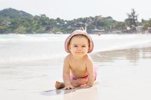 lächelndes kleines Mädchen spielt mit Sand in der Nähe des Meeres auf dem Hintergrund eines tropischen Strandes. foto