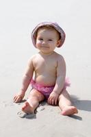 lächelndes kleines Mädchen in rosafarbener Badehose, das am Strand mit Sand spielt. sensorische Entwicklung für Kinder im Freien. foto