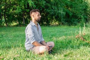 Porträt eines jungen gutaussehenden europäischen Mannes in Freizeitkleidung, der im Sommerpark auf einem Gras sitzt. foto