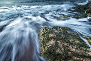 malerische seelandschaft eines großen felsens und wellen, die herausfließen foto