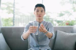 hübscher junger mann, der ein glas wasser und eine pille in der hand hält. foto