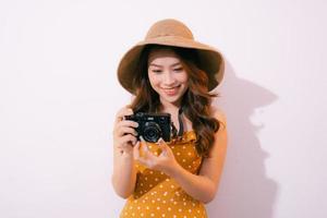 Nahaufnahme Porträt eines lächelnden hübschen Mädchens im Kleid, das ein Foto auf einer Retro-Kamera macht, die über rosafarbenem Hintergrund isoliert ist