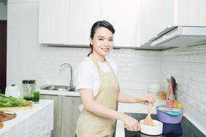 junge frau, die nahe dem induktionsherd steht, der mahlzeit in der küche kocht foto