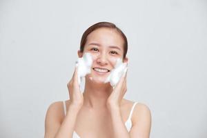 glückliche asiatische Frau wäscht ihr Gesicht mit Seifenschaum auf weißem Hintergrund. foto