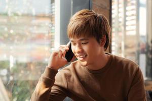 lächelnder junger Mann sitzt im Café und telefoniert mit dem Handy. foto