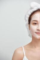 Porträt einer jungen attraktiven Asiatin mit Gesichtsmaske aus Ton auf weißem Hintergrund.