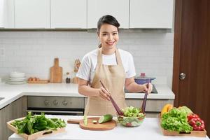 glückliche junge Hausfrau, die Gemüsesalat mischt foto