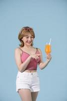 sommerporträt einer schönen asiatischen frau, die fruchtsaftgetränk isoliert auf pastellblauem hintergrund hält foto