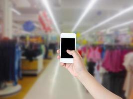 Hand, die Handy mit Supermarktregalgang hält, verschwommenen Hintergrund foto