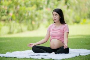 eine schwangere asiatin entspannt sich mit yoga-dehnübungen im park für die gesundheit der mutter und des ungeborenen kindes foto