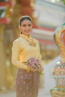 attraktive thailändische frau in einem alten thailändischen kleid hält frische blumen, die buddha huldigen, um sich auf dem traditionellen songkran-fest in thailand etwas zu wünschen foto