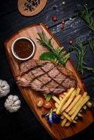 gegrilltes Rindersteak mit Gewürzen und Pommes frites auf einem Holzschneidebrett foto