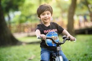 bangkok thailand - oktober 09, 2016 glücklicher fröhlicher kindjunge, der fahrrad im park in der natur fährt foto