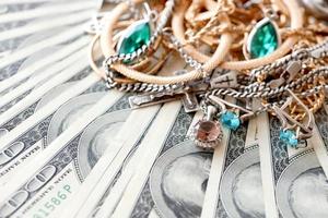 Viele teure goldene und silberne Schmuckringe, Ohrringe und Halsketten auf einer großen Menge von US-Dollar-Scheinen aus nächster Nähe. Pfandhaus oder Juweliergeschäft foto