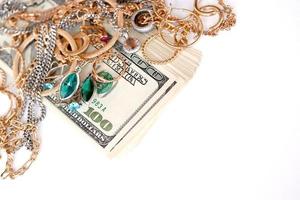 Viele teure goldene und silberne Schmuckringe, Ohrringe und Halsketten mit einer großen Menge US-Dollar-Scheine auf weißem Hintergrund. Pfandhaus oder Juweliergeschäft foto