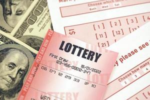 Rotes Lotterielos liegt auf rosa Glücksspielbögen mit Zahlen zum Markieren auf großen Hundert-Dollar-Scheinen. lotteriespielkonzept oder spielsucht. Nahansicht foto