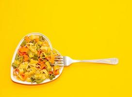 Herzförmiger Teller voller farbiger Nudeln auf gelbem Hintergrund mit einer Gabel. Food-Konzept. richtige Ernährung. foto