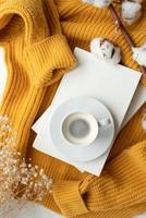 gemütliche komposition aus warmem gelbem pullover, weißen büchern, tasse heißem kaffee und trockenen blumen, draufsicht foto