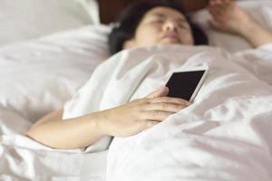 Frau, die im Bett schläft und ein Handy hält.