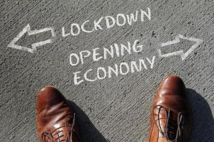 zwei Lederschuhe vor den Worten Lockdown und Opening Economy und Pfeile, die in entgegengesetzte Richtungen zeigen foto