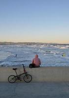 Person mit Fahrrad von hinten gesehen auf einer Mauer an der Küste von Valencia, Spanien foto