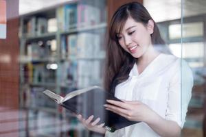 asiatische schöne Studentin, die Buch im Bibliotheksporträt hält foto