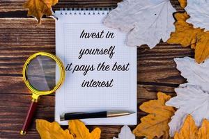 investieren Sie in sich selbst, es bringt die besten Zinsen, der Text ist in ein weißes Notizbuch geschrieben, mit einem Stift auf einem Hintergrund aus Herbst, Ahorn, Blättern und alten Brettern. foto