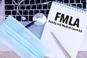 Fmla Family Medical Leave Act, der Text ist in ein Notizbuch geschrieben, neben einem Stift, einer medizinischen Einwegmaske und einem Laptop auf Leinenhintergrund. foto