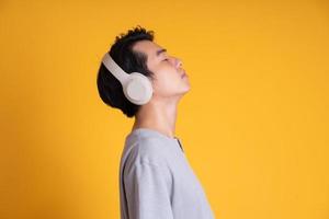Bild eines asiatischen Mannes, der Musik mit Kopfhörern hört, isoliert auf gelbem Hintergrund foto