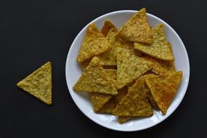 Mexikanische Nachos-Maischips mit Pfeffer auf einem weißen Teller auf schwarzem Hintergrund. leckeres frühstück mit gepfefferten nachos. foto