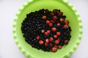 Erdbeeren und schwarze Johannisbeeren in einer grünen Platte. foto