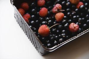 Erdbeeren und schwarze Johannisbeeren in Plastikbehältern. köstliche frische Beeren in einer Box auf weißem Hintergrund. foto