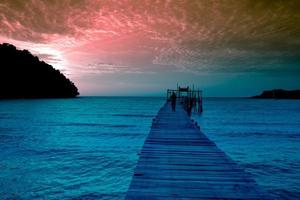 Ein hölzerner Pier, der sich bis zum Meer erstreckt, Meerblick, Sonnenuntergang mit Bergen und bewölktem Himmel für Reisen im Urlaub, Entspannungszeit im Sommer foto