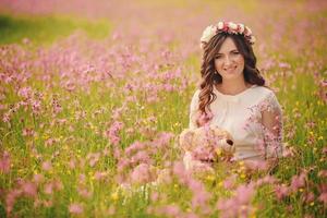 Porträt einer schwangeren Frau mit Teddybär im Feld von rosa Blumen. junge schöne schwangere Mädchen mit einem Kranz auf dem Kopf in der Sonne. Mutterschaft. Frühling. Platz kopieren. selektiver Fokus foto