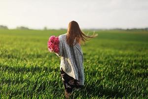 schöne junge Frau auf einem Spaziergang, das Mädchen in Blumen. Strauß Pfingstrose. elegante junge frau mit wunderschönem haar. Ein Mädchen mit Pfingstrose geht auf dem Feld spazieren. foto