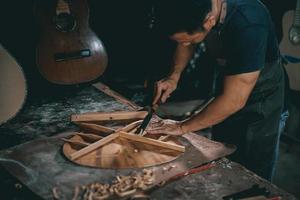 Gitarrenbauer asiatischer Mann, der Akustikgitarren im Labor herstellt. asiatischer gitarrenbauer baut hochwertige gitarren für musiker handgefertigter gitarrenshop. Arbeiten mit feiner Holzmusik, Tradition, altem Handwerk. foto