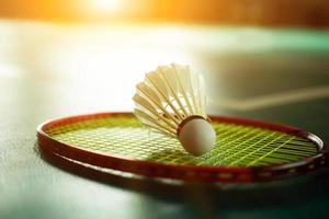 Cremeweißer Badmintonfederball und Schläger mit Neonlichtschattierung auf grünem Boden im Indoor-Badmintonplatz, verschwommener Badmintonhintergrund, Kopierraum. foto