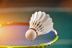 Cremeweißer Badmintonfederball und Schläger mit Neonlichtschattierung auf grünem Boden im Indoor-Badmintonplatz, verschwommener Badmintonhintergrund, Kopierraum. foto