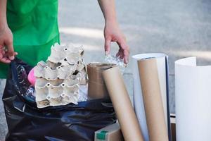 hausbesitzer trennt flaschen, papier, eierkartons und andere stoffe in der schwarzen plastiktüte vor dem haus, konzept zur reduzierung der globalen erwärmung, zur rettung unserer welt, weicher und selektiver fokus. foto