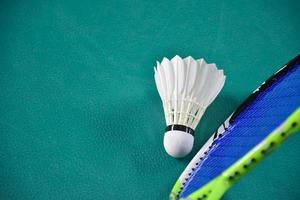 Cremeweißer Badmintonfederball und Schläger mit Neonlichtschattierung auf grünem Boden im Indoor-Badmintonplatz, verschwommener Badmintonhintergrund, Kopierraum. foto