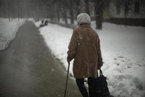 Frau geht im Schnee die Straße hinunter. Rentner im Winter in der Stadt. Frau lehnt sich auf Stock. foto