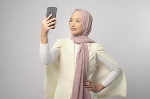 Schöne muslimische Frau mit Hijab mit Smartphone auf weißem Hintergrund, Technologiekonzept. foto