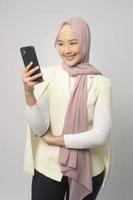 Schöne muslimische Frau mit Hijab mit Smartphone auf weißem Hintergrund, Technologiekonzept. foto