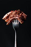 In Scheiben geschnittenes gegrilltes Steak medium rare auf der Gabel, Nahaufnahme, schwarzer Hintergrund. foto