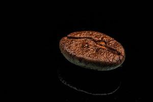 eine einzelne Kaffeebohne Makroaufnahme mit Wassertropfen und Reflexion. schwarzer Hintergrund foto