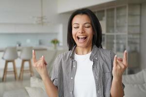 Aufgeregte coole junge Frau zeigt Hardrock-Handgeste und schreit zu Hause singen. Erfolg, Glück foto