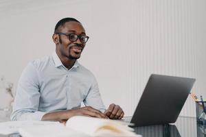 lächelnder afroamerikanischer mann, der an einem geschäftsprojekt am laptop arbeitet und e-mails mit guten nachrichten liest foto